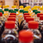 Mehrere PET-Getränkeflaschen mit roten, grünen und gelben Verschlüssen stehen dicht nebeneinander in einem Supermarktregal. Zu sehen sind verschiedene Softdrinks und Erfrischungsgetränke in Kunststoffflaschen.
