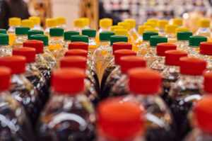 Mehrere PET-Getränkeflaschen mit roten, grünen und gelben Verschlüssen stehen dicht nebeneinander in einem Supermarktregal. Zu sehen sind verschiedene Softdrinks und Erfrischungsgetränke in Kunststoffflaschen.