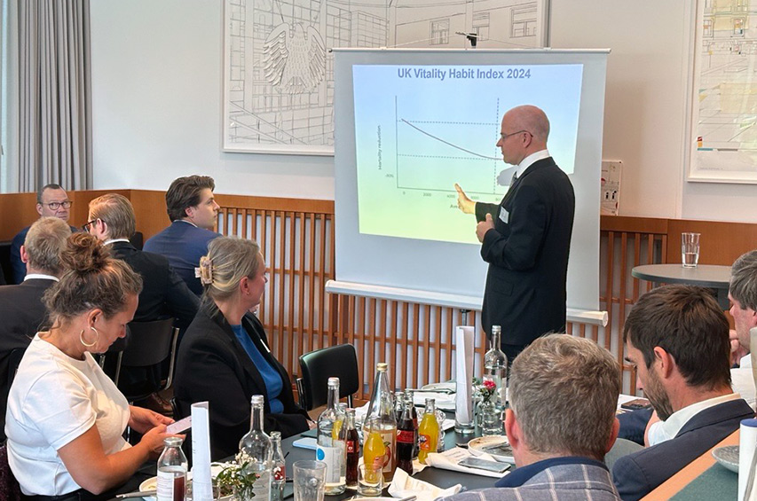 Prof. Dr. Boris Bigalke präsentiert vor Sitzungsteilnehmern eine Folie mit dem Titel "UK Vitality Habit Index 2024".