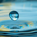 Wassertropfen fällt auf Wasseroberfläche und erzeugt konzentrische Wellen