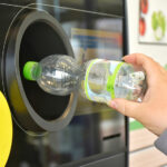 Hand gibt eine leere PET-Flasche in einen Pfandautomaten zurück.