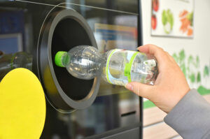 Hand gibt eine leere PET-Flasche in einen Pfandautomaten zurück.
