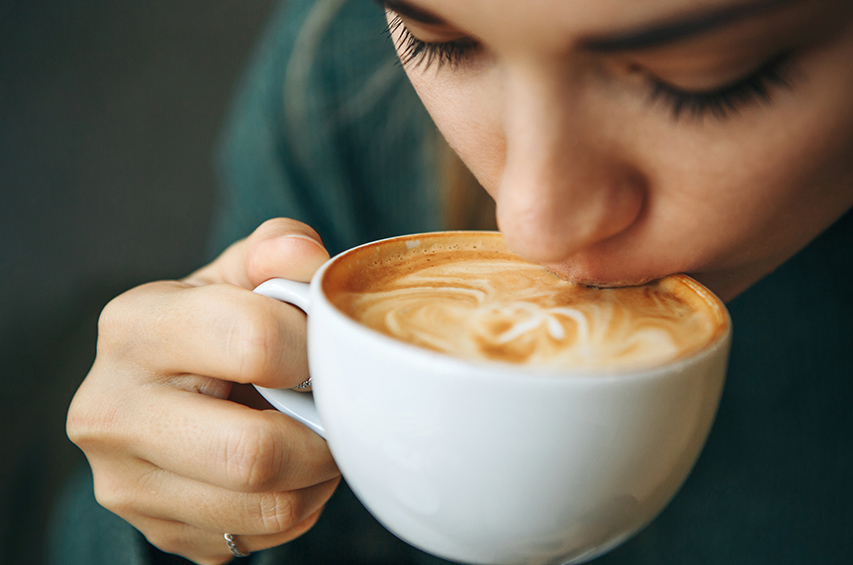 Frau trinkt eine Tasse Cappuccino mit Herz-Latte-Art