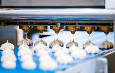 Automatisierte Dosiermaschine trägt Teigportionen auf ein Förderband in einer Lebensmittelproduktion auf.