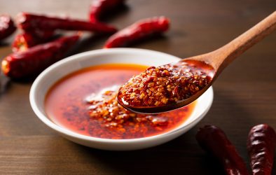 Löffel mit Chiliöl und Chiliflocken über einer Schale mit scharfer Sauce