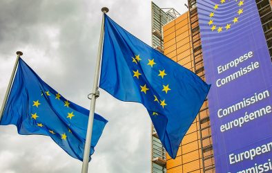 Europäische Unionsflaggen vor dem Gebäude der Europäischen Kommission unter einem bewölkten Himmel