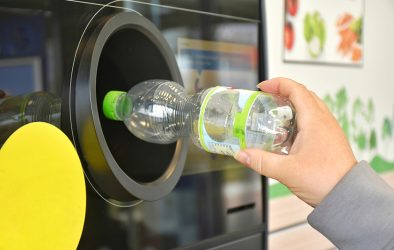 Hand gibt eine leere PET-Flasche in einen Pfandautomaten zurück.