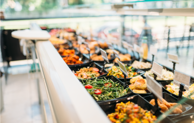 "Frische Salatbar in einem Selbstbedienungsrestaurant mit verschiedenen Schüsseln gefüllt mit Salaten, Gemüse, Brot und anderen Beilagen. Kleine Schilder mit Beschriftungen stehen vor den Speisen.