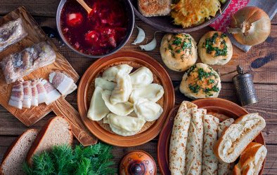 Tisch mit osteuropäischen Speisen wie Teigtaschen, Suppe und Brot.
