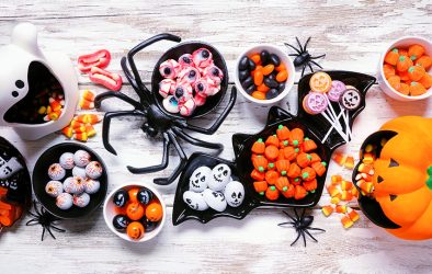 Halloween-Süßigkeiten in Schalen, dekoriert mit Kürbis- und Gruselmotiven auf einem Tisch.
