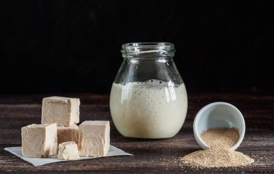 Frische Würfelhefe, flüssige Hefe im Glas und Trockenhefe in einer Schale auf einem Holztisch