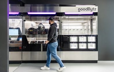 Ein Mitarbeitender steht vor der GoodBytz-Kochstation, in der Roboterarme Zutaten verarbeiten und Gerichte zubereiten.