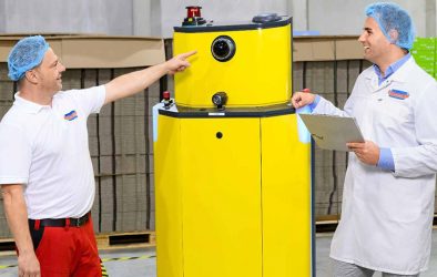 Zwei Mitarbeiter in Hygienekleidung stehen in einer Produktionshalle.
