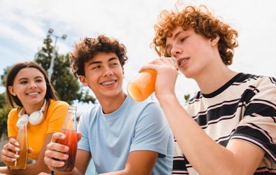 Drei Jugendliche trinken Limonade aus Glasflaschen im Freien.