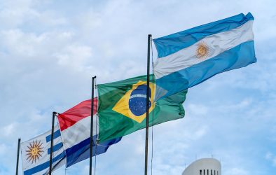 Flaggen der MERCOSUR-Staaten (Uruguay, Paraguay, Brasilien und Argentinien) wehen im Wind vor blauem Himmel