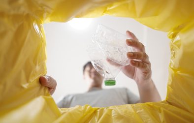 Verbraucher wirft leere Plastikflasche in eine gelbe Tonne zur Mülltrennung