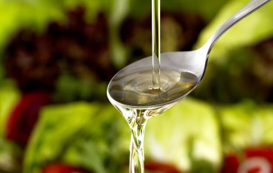 Speiseöl läuft in einen Löffel vor frischem Salat