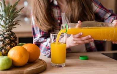 Frau gießt Orangensaft aus Plastikflasche in ein Glas.