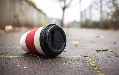 Weggeworfener Einweg-Kaffeebecher liegt auf einem nassen Gehweg.