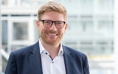 Tobias Koppitz im Porträt – lächelnd, mit Brille und Business-Outfit.
