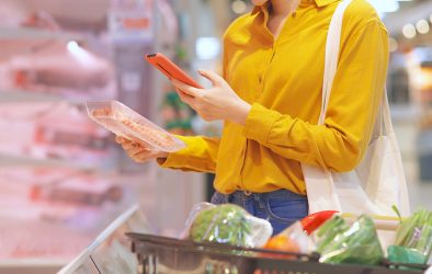 Frau scannt Lebensmittelverpackung mit Smartphone im Supermarkt
