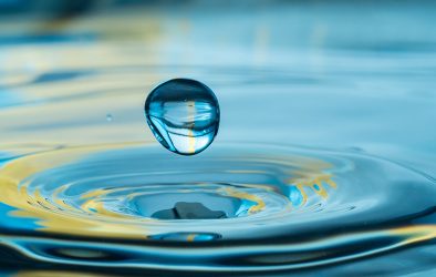 Wassertropfen fällt auf Wasseroberfläche und erzeugt konzentrische Wellen